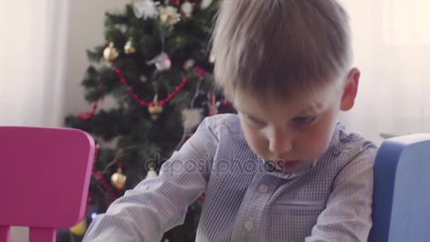 Мальчик рядом с рождественской ёлкой что-то делает — стоковое видео