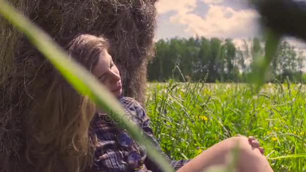 Jonge vrouw zittend op het gras in de buurt van hooiberg — Stockvideo