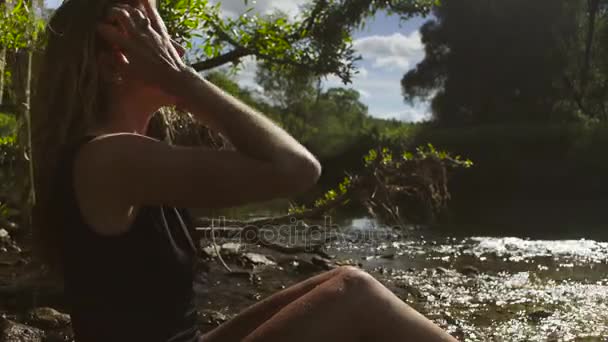 Ung kvinna sitter i en flod i grunt vatten — Stockvideo