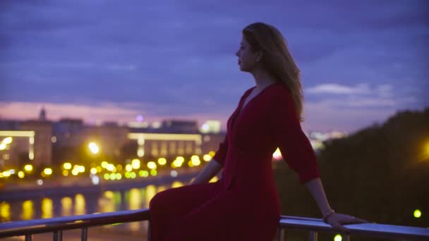 Mujer joven en vestido rojo está sentado en un parapeto — Vídeos de Stock