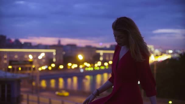 Ung kvinna i röd klänning sitter på ett räcke — Stockvideo