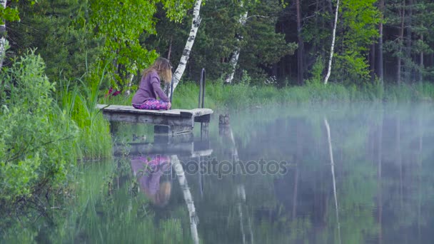 Vrouw doen yoga oefeningen op de oever van het meer — Stockvideo