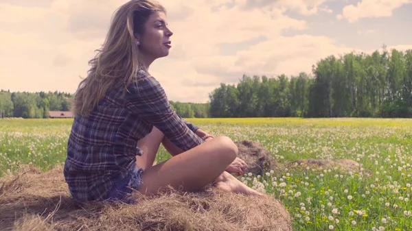 Young woman sitting on haystack at summer — Stock Photo, Image