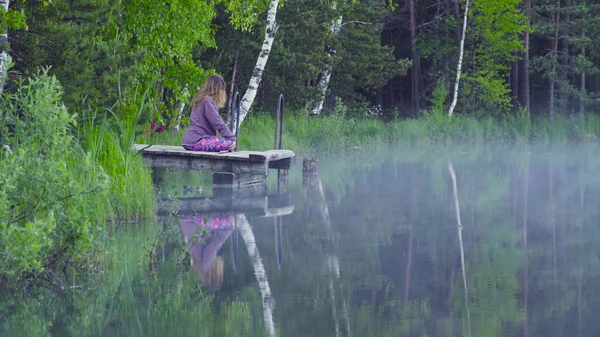 Fiatal nő, egy tó partján meditál — Stock Fotó