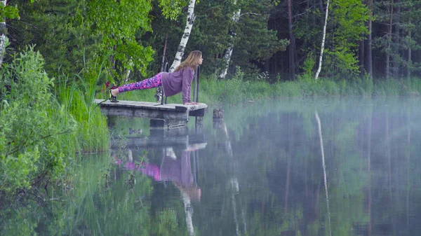 Fiatal nő csinál jóga gyakorlatok, a tó partján — Stock Fotó