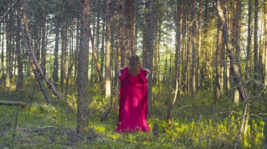 Kırmızı elbiseli genç bir kadın ormanda yürüyor.
