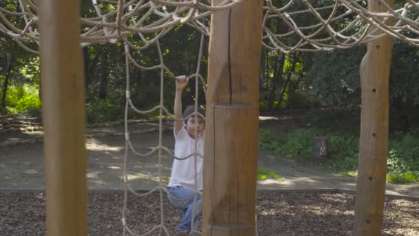 En pojke som klättring på en lekplatsutrustning — Stockvideo
