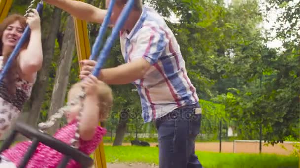 Hombre balanceando a su hija y su esposa en un columpio — Vídeos de Stock