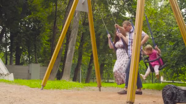 Hombre balanceando a su hija y su esposa en un columpio — Vídeos de Stock