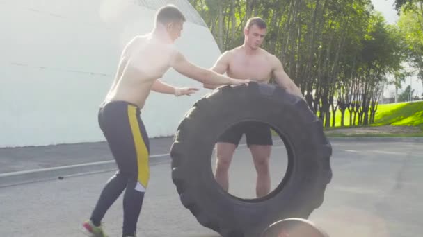 Два молодых человека катают колесо, чтобы делать упражнения по кроссфиту. — стоковое видео