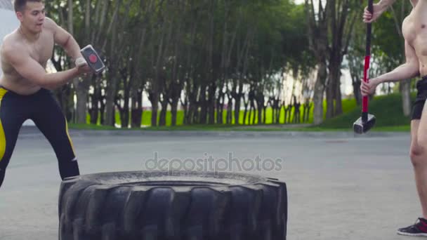 Two young men doing exercises on a large wheel and hammer — Stock Video