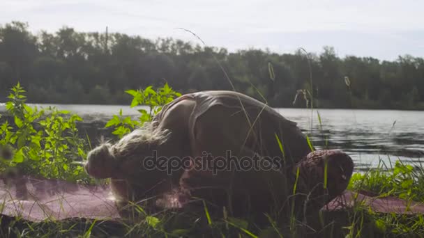 Femme faisant des exercices de yoga sur la rive de la rivière — Video