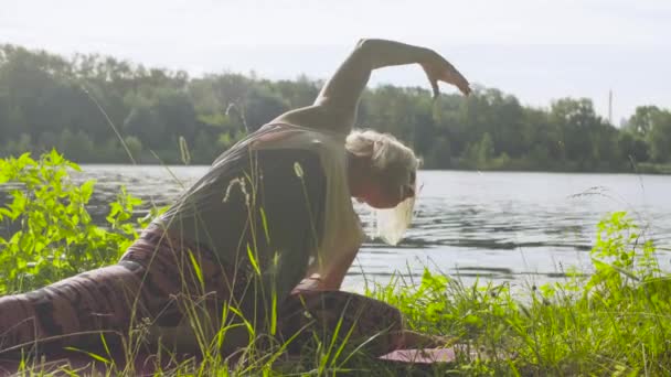 Žena, která dělá cvičení jógy na břehu řeky — Stock video
