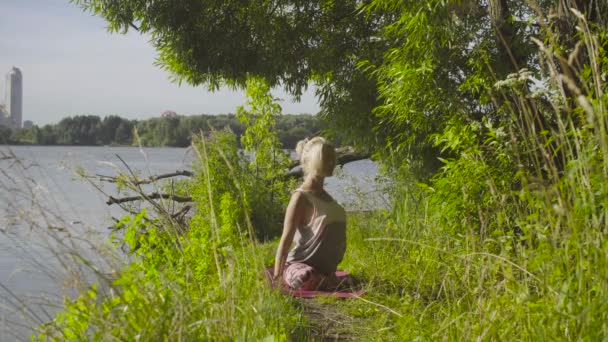 Mujer haciendo ejercicios de yoga en la orilla del río — Vídeo de stock