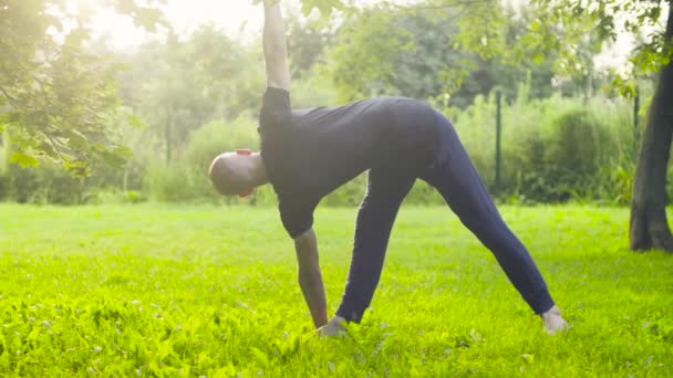 Een man doen yoga oefeningen in het park — Stockvideo