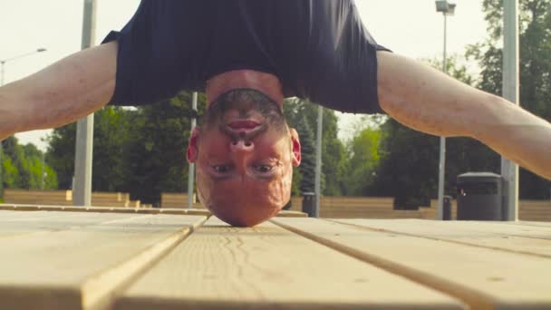 Gezicht van een man doen headstand in het park — Stockvideo