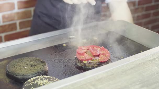 Händerna på kocken att sätta tomater på en grillad hamburgare — Stockvideo