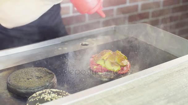 Manos de chef vertiendo salsa en una hamburguesa a la parrilla — Vídeos de Stock