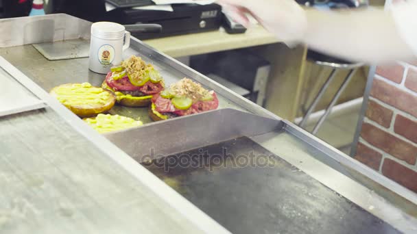 Mãos de chef pondo salada em um hambúrguer pronto — Vídeo de Stock