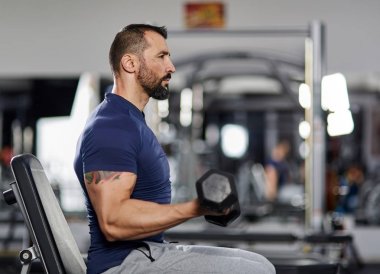 Pazı kıvırmak salonunda dumbbells ile yapan erkek
