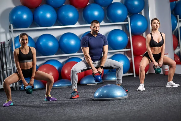 Fitness instructor with two girls working out with kettlebell