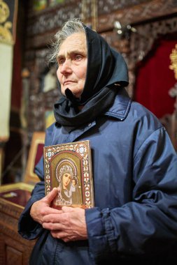 Bir dinsel simge/ikon bir kilise içinde tutan yaşlı köylü kadın