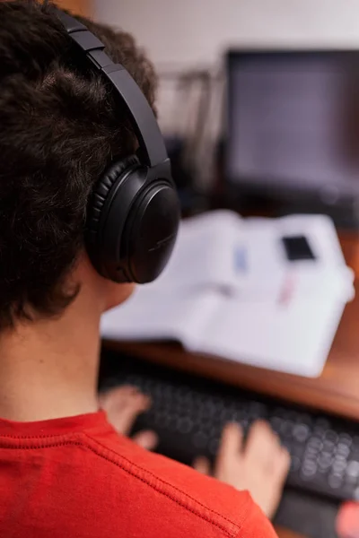 ヘッドフォンで音楽を聴きながら宿題をしている若い学生 — ストック写真