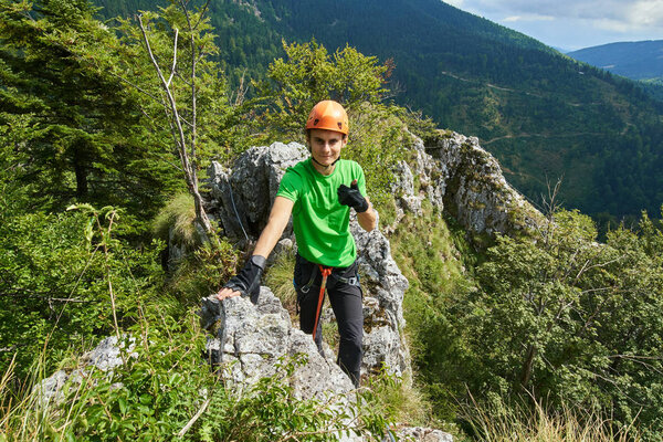 Young man wearing protective mountaineering gear showing thumbs up sign while climbing