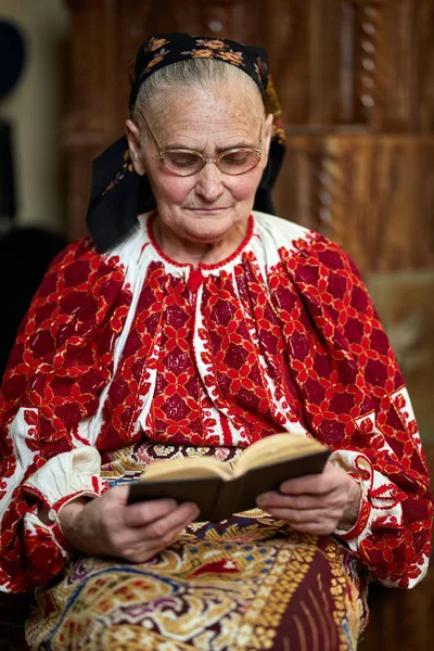 Ηλικιωμένη Γυναίκα Φορώντας Παραδοσιακή Ενδυμασία Και Γυαλιά Ανάγνωσης Βιβλίου Εσωτερική — Φωτογραφία Αρχείου