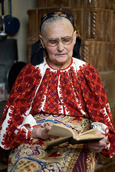 伝統的な衣装や屋内の本を読んで眼鏡を身に着けている老婆 — ストック写真