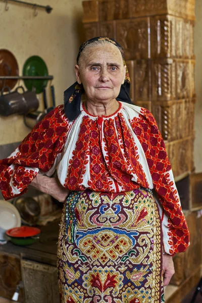 ストーブ近くに立っている伝統的な衣装に身を包んだ老婆ルーマニア — ストック写真