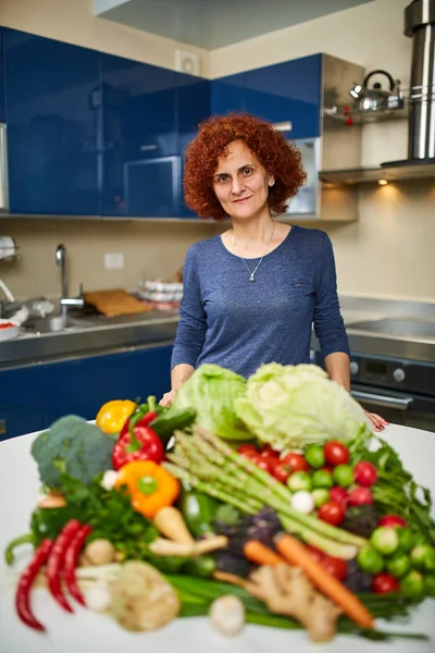 Mujer con una gran pila de verduras en la mesa — Foto de Stock