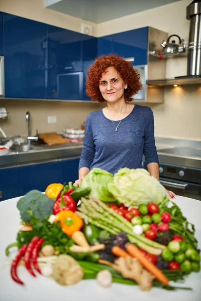 Mujer con una gran pila de verduras en la mesa —  Fotos de Stock