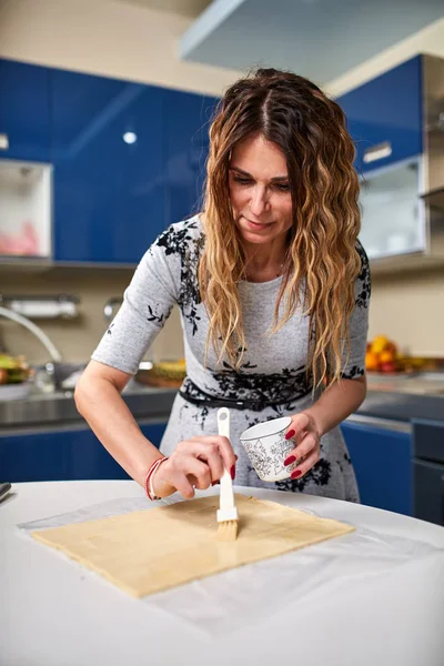 Mature woman spreading dough in kitchen at home
