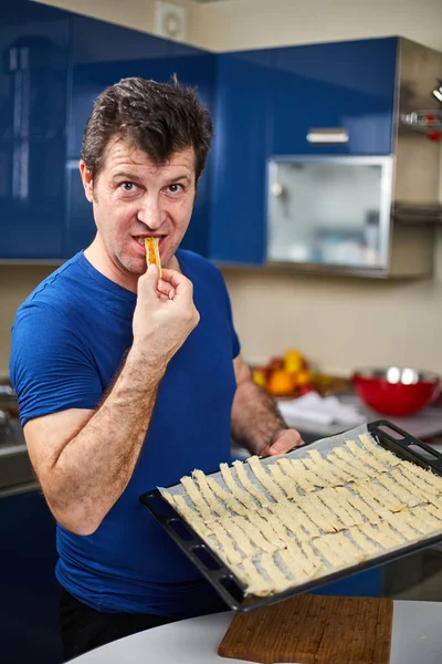 Man tasting cheese cracker and holding tray full of raw crackers the kitchen