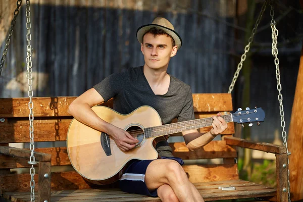 Guapo Joven Tocando Guitarra Mientras Está Sentado Swing Aire Libre — Foto de Stock