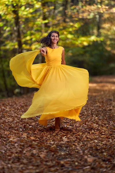 快乐的年轻女子穿着长长的黄色衣服在秋天的风景中跳舞 — 图库照片