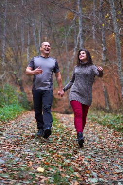 Ormanda yapraklarla kaplı bir sokakta yürüyen çift.