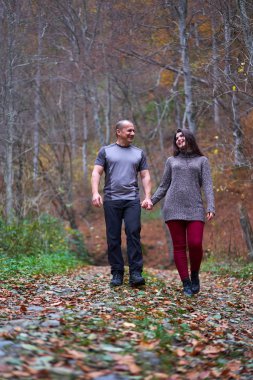 Ormanda yapraklarla kaplı bir sokakta yürüyen çift.