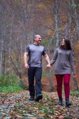 Ormanda yapraklarla kaplı bir sokakta yürüyen çift.