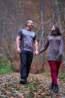 Ormanda yapraklarla kaplı bir sokakta yürüyen çift.