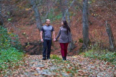 Ormanda yapraklarla kaplı bir sokakta yürüyen çift.