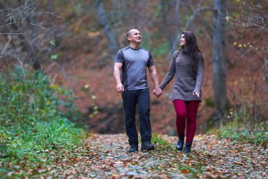 Ormanda yapraklarla kaplı bir sokakta yürüyen çift.