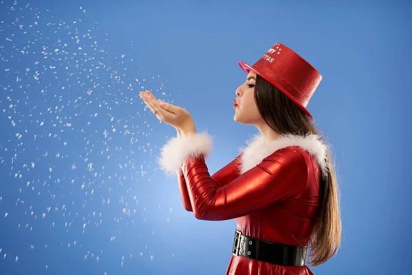 サンタの女の子は青い背景を背景に雪の結晶を吹いて — ストック写真