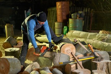 Oduncu gece geç saatlere kadar çalışıyor. Elektrikli testereyle kütükleri kesiyor.