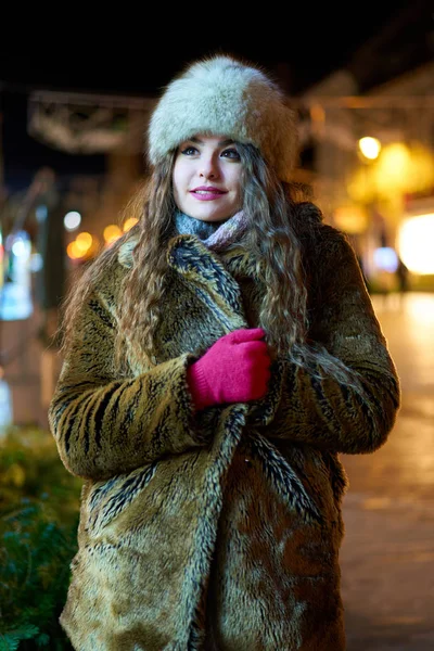A young woman at night time with city lights behind