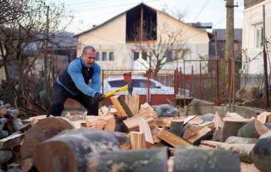 Kırsal adam arka bahçesinde balta ve pençe ile odun kırıyor.