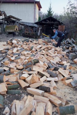 Kırsal adam arka bahçesinde balta ve pençe ile odun kırıyor.