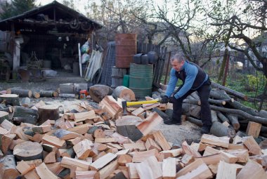 Kırsal adam arka bahçesinde balta ve pençe ile odun kırıyor.