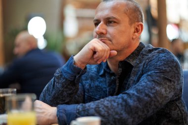 Barda bir masada oturan orta yaşlı bir adam.